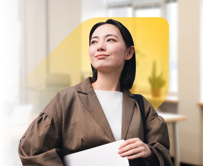 Une photo d’une femme asiatique souriant fièrement, superposée sur le losange étendu de la Banque EQ et un espace de bureau lumineux avec des plantes en pot.